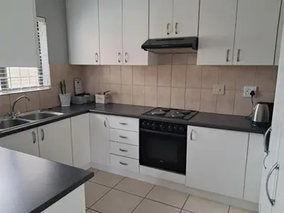 a kitchen with white cabinets and a black stove top oven at 8 Marina Sands beach apartment in Cape Town