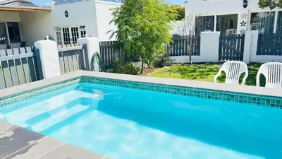 a swimming pool with two chairs and a house at Hermanus Garden Studios in Hermanus