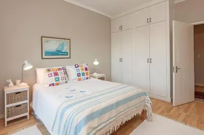 a white bedroom with a bed and a white cabinet at Whispering Waves in Hermanus