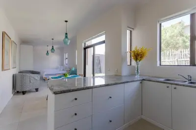 a kitchen with white cabinets and a sink at Lux Private Garden Studio - Sunset Beach in Cape Town