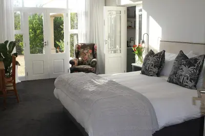 a bedroom with a large white bed and a chair at Jakaranda Cottage in Somerset West