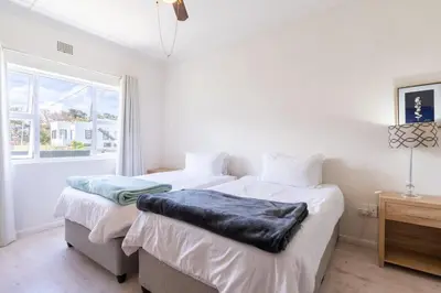 a white bedroom with two beds and a window at Coastal Elegant 4 Bedroom Home in Hermanus