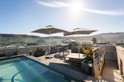 a balcony with a swimming pool and umbrellas at Ocean Family Deluxe, Hermanus Waterfront Apartments in Hermanus