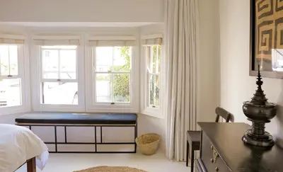 a bedroom with a bed and a desk and windows at Kumbuk House in Franschhoek