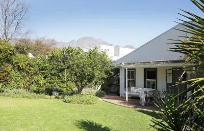 a white house with a garden and a house at Kumbuk House in Franschhoek