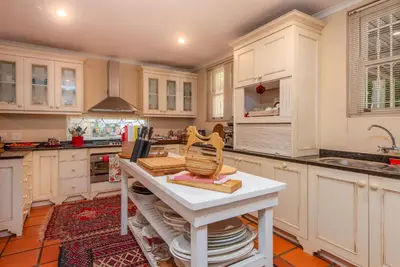 a kitchen with white cabinets and a white table at Beautiful country house set in lush garden in Wellington