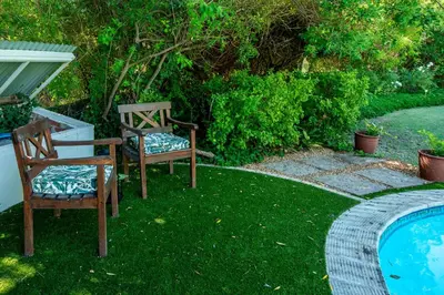 two chairs sitting in the grass next to a swimming pool at Beautiful country house set in lush garden in Wellington