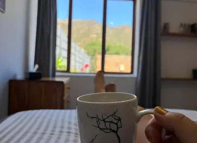 a person is holding a coffee cup on a table at Mountain Views, beach walks, heart of old village in Gordonʼs Bay