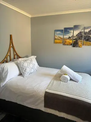 a bedroom with a white bed with four paintings on the wall at Mountain Views, beach walks, heart of old village in Gordonʼs Bay