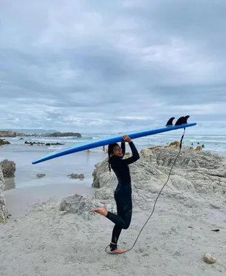 a woman carrying a surfboard on the beach at Awesome room in surf house in Hermanus