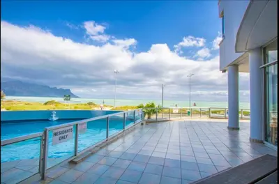 a building with a swimming pool next to the ocean at Sunset Accommodation in Strand in Strand