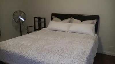a bedroom with a bed with white sheets and a fan at Ocean Elephant Beach Apartment LONG TERM in Strand