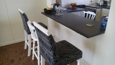 a kitchen with a black counter top and white chairs at Ocean Elephant Beach Apartment LONG TERM in Strand