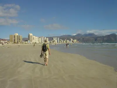 a man walking on the beach with a backpack at Ocean Elephant Beach Apartment LONG TERM in Strand