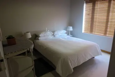 a bedroom with a bed with white sheets and a window at Hidden gem in bush 350m from main beach in Bettyʼs Bay