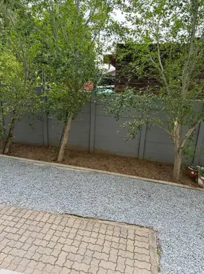 a backyard with a fence and trees and a brick driveway at Slaap Self Catering in Paarl