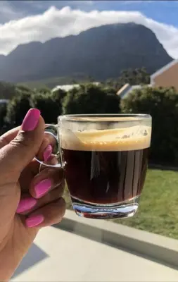 a person holding a glass of coffee with a mountain at C'est la Vie 2 in Franschhoek