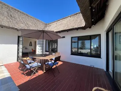 a patio with a table and chairs and an umbrella at Lala Panzi House - Grotto Beach, Voëlklip in Hermanus