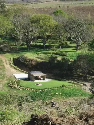 a small building on a green field with trees at Babylons Tower Shepherds Hut in Mosselrivier