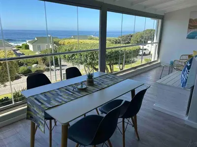 a table and chairs in a room with a view of the ocean at 24 Whale Rock Estate in Hermanus
