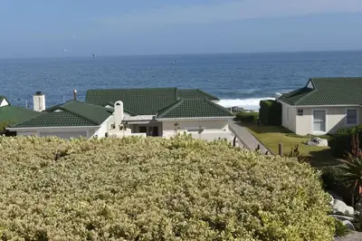 a white house with the ocean in the background at 24 Whale Rock Estate in Hermanus