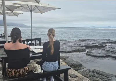 two women sitting on a bench looking at the ocean at A Short Walk to the Cliffs in Hermanus