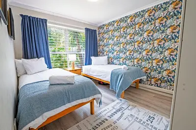 a bedroom with two beds and a window with blue curtains at Cozy Garden Unit in Bloubergstrand in Bloubergstrand