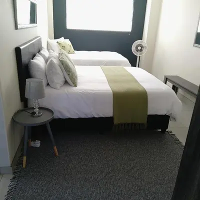 a bedroom with two beds and a table with a lamp at 1 On Sonnet Unit Elaine in Cape Town