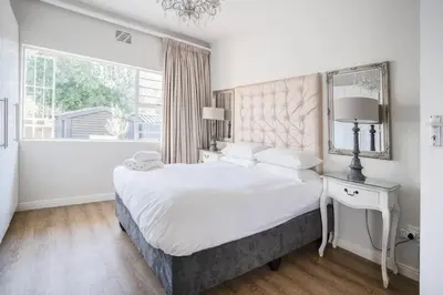 a white bedroom with a large bed and a window at Avemore Vredehof 1 with backup power in Stellenbosch