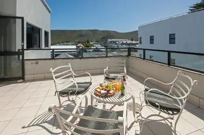a balcony with chairs and a table with a bowl of fruit at Seafront Penthouse - Marine Court Hermanus in Hermanus