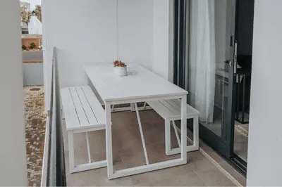 a white table and bench next to a window at Calm Blouberg Beach Apt - Gated & Lift Access in Cape Town