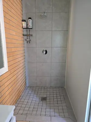 a bathroom with a shower with a tiled floor at Red Door Strand Guest house in Cape Town