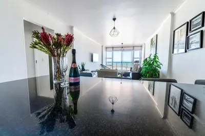 a bottle of wine and flowers on a table in a living room at Luxury Beachfront Apartment in Blouberg, 304 The Waves in Bloubergstrand