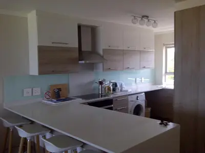 a kitchen with white cabinets and a counter with stools at Beachfront Apartment at Seaspray in Blouberg in Bloubergstrand