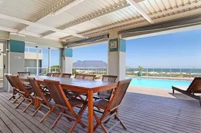 a dining room with a table and chairs and a pool at Beachfront Apartment at Seaspray in Blouberg in Bloubergstrand
