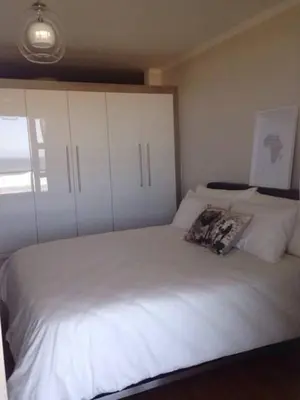 a bedroom with a white bed with white cabinets at Beachfront Apartment at Seaspray in Blouberg in Bloubergstrand