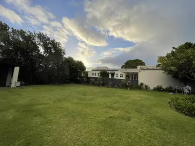 a yard with a white building and a grass field at Mosselberg Garden Gottage in Hermanus