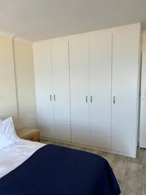 a bedroom with white cabinets and a bed at Nautica by the Beach in Cape Town