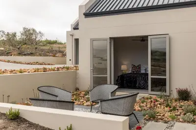 a patio with three chairs and a bed in a bedroom at Oceanique in Hermanus