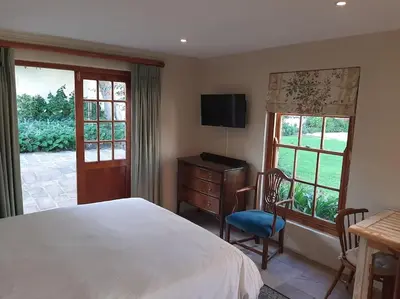 a bedroom with a bed and a desk and windows at Klein La Cotte Garden Cottage in Franschhoek