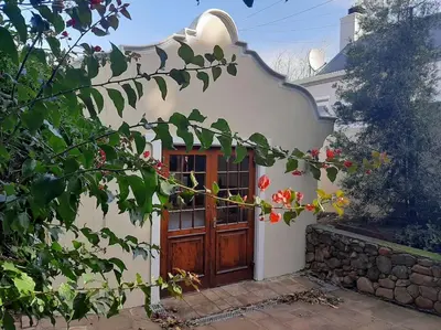 a house with a wooden door and some flowers at Klein La Cotte Garden Cottage in Franschhoek