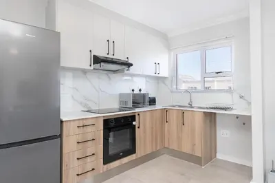 a kitchen with white appliances and wooden cabinets at Elegant apartment near beach in Cape Town