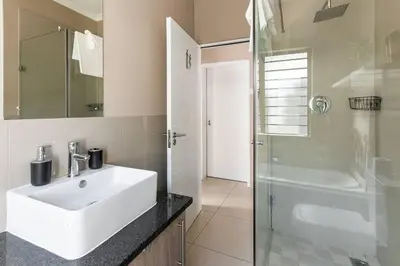 a bathroom with a white sink and a shower at The Greenfields Suite in Cape Town