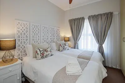 a white bedroom with a large bed and a window at Unwind at Coral 2BR Bloubergstrand Beach Apt Walk to Beach in Bloubergstrand