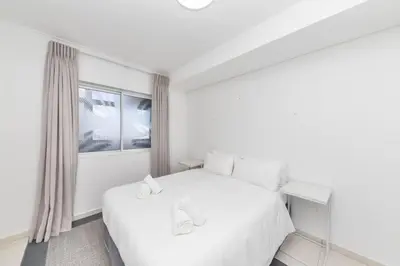 a white bedroom with a white bed and a window at Horizon Bay 202 Beachfront APT, Bloubergstrand in Cape Town