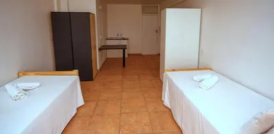 a room with two beds and a kitchen with a table at Montana Backpackers Cape Town in Cape Town