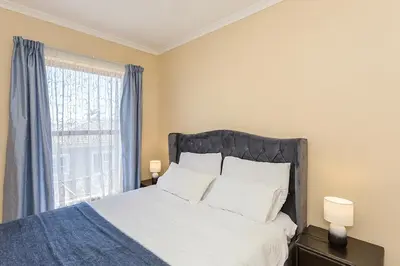 a bedroom with a bed with white sheets and a window at Secured 3-Bedroom Townhouse in Cape Town