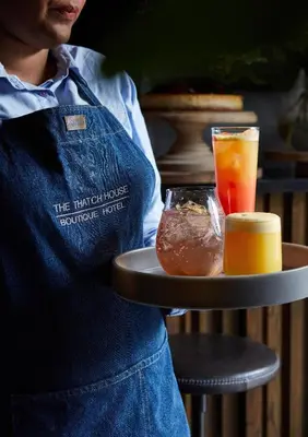 a person holding a tray with a drink and a tray of food at The Thatch House Boutique Hotel, Hermanus in Hermanus