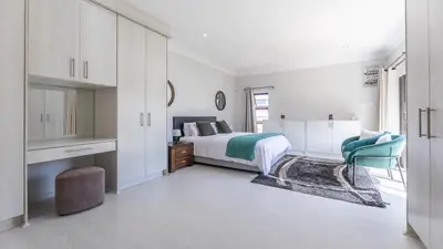 a white bedroom with a bed and a chair at Paraiso - A cozy retreat , your home away from home in Cape Town
