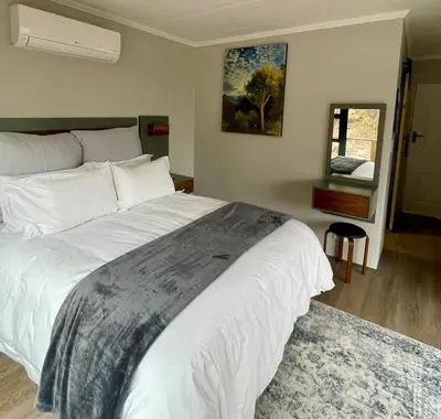 a bedroom with a large white bed and a mirror at Stonehedge Cottages in Franschhoek